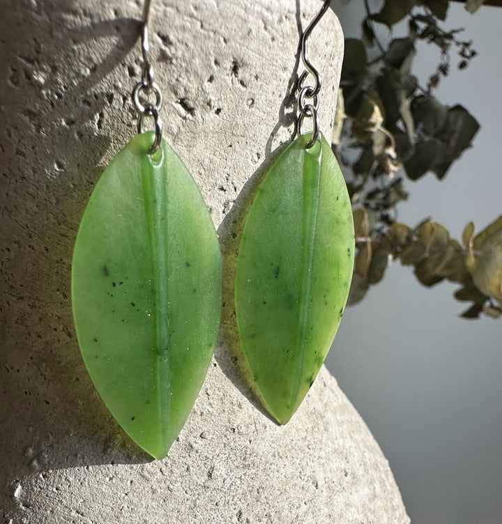 Close up of jade leaf earrings showing bright green elongated leaves on metal ear wires.