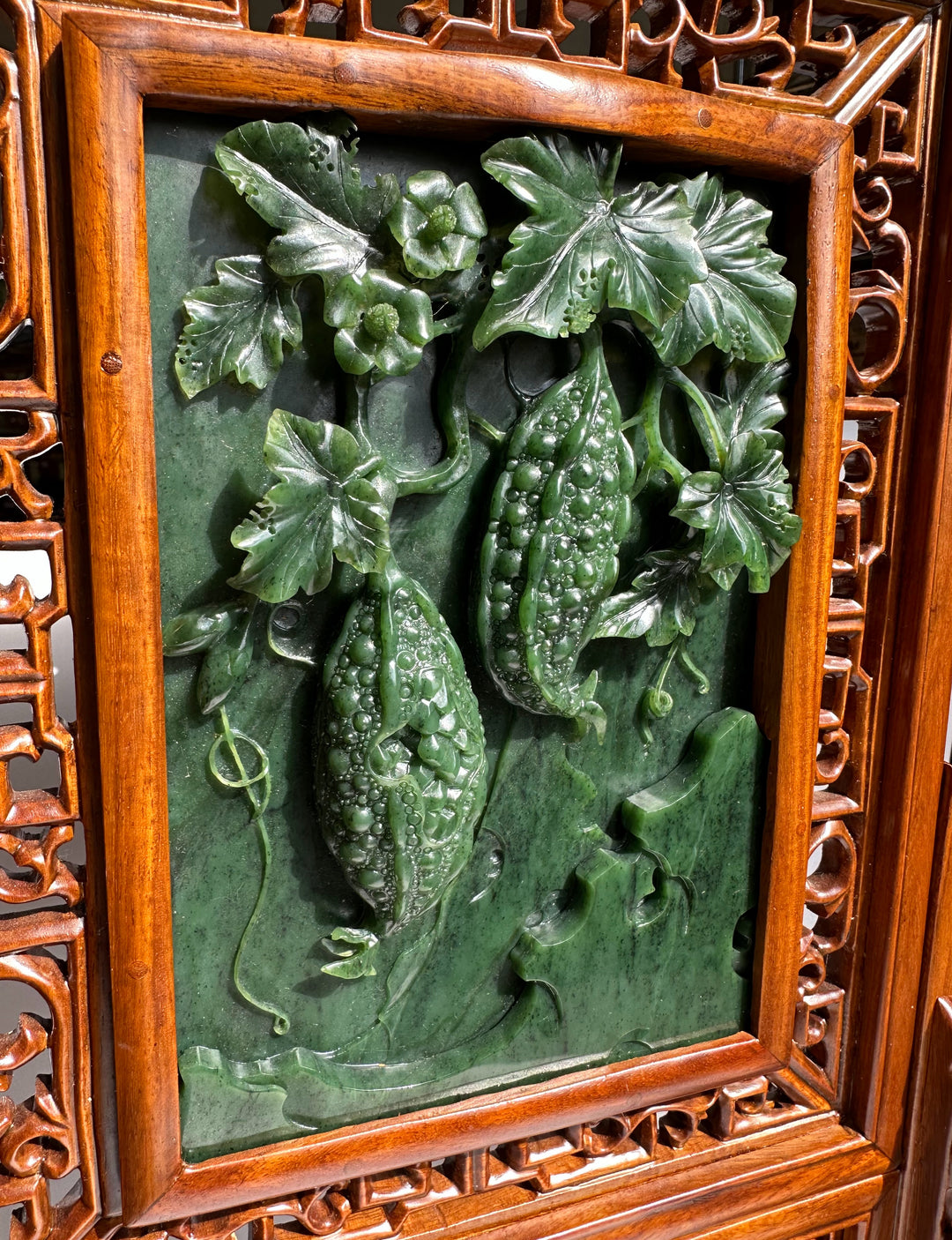 Close-up of jade carving showing two gourds entwined with leaves on a green background within a carved wooden frame