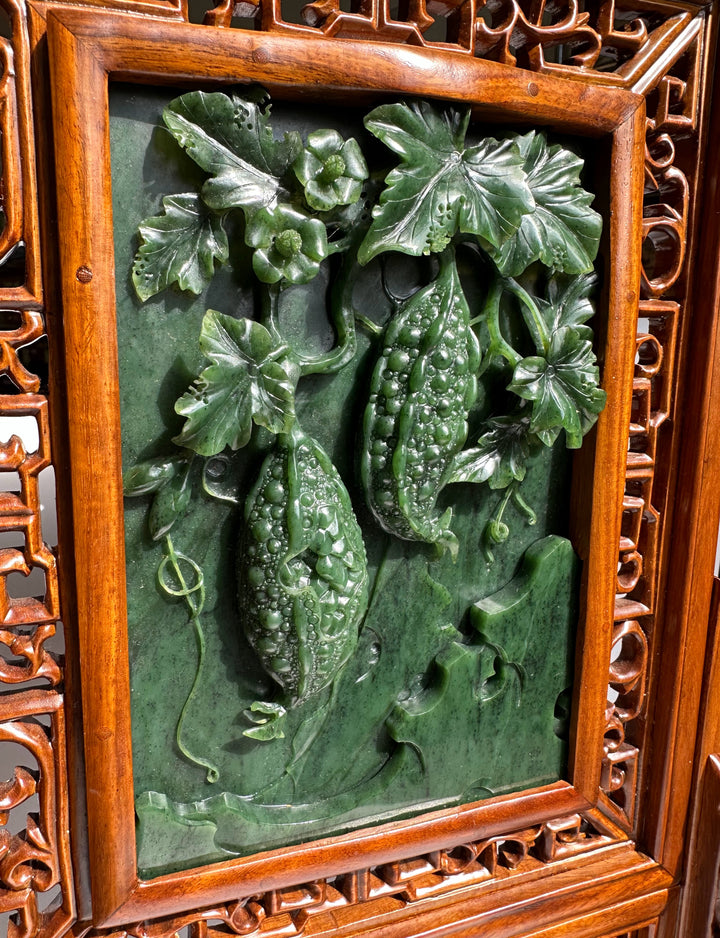 Close-up of jade carving showing two gourds entwined with leaves on a green background within a carved wooden frame