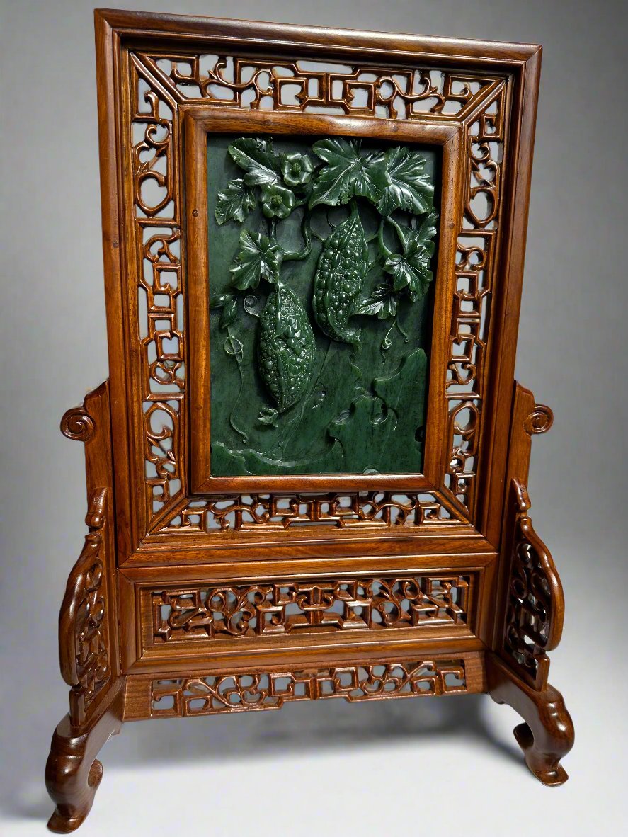 Jade panel carved with gourds and leaves framed by an ornate carved wooden screen on a stand