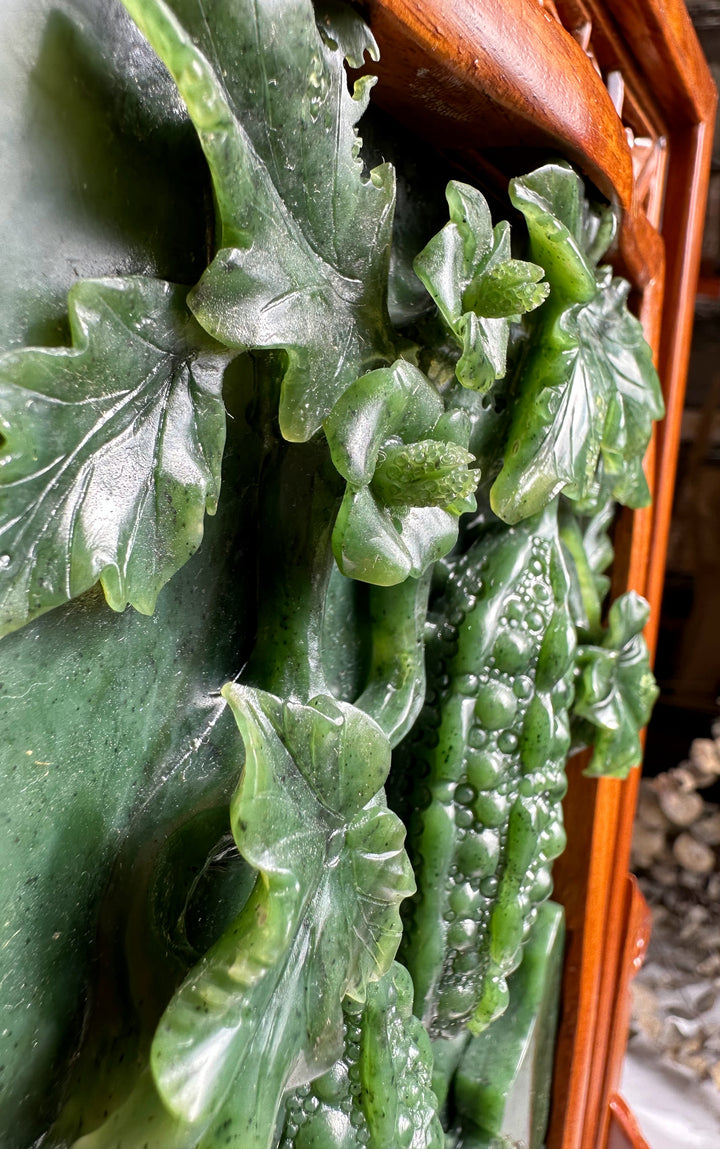 Close up of jade carving showing detailed leaves and gourds on deep green jade panel.