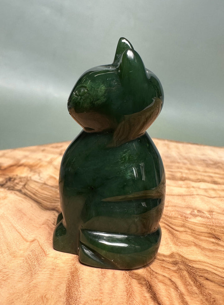 Rear three-quarter view of emerald green jade cat figurine on a wooden surface