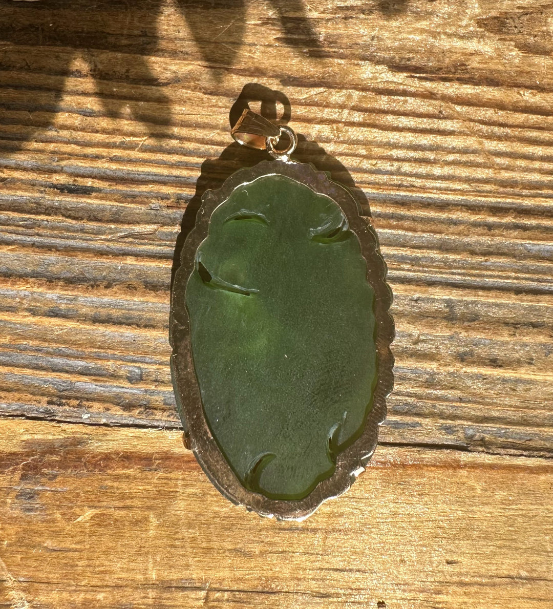 Back view of vintage jade Guanyin pendant with scalloped bronze frame on wood