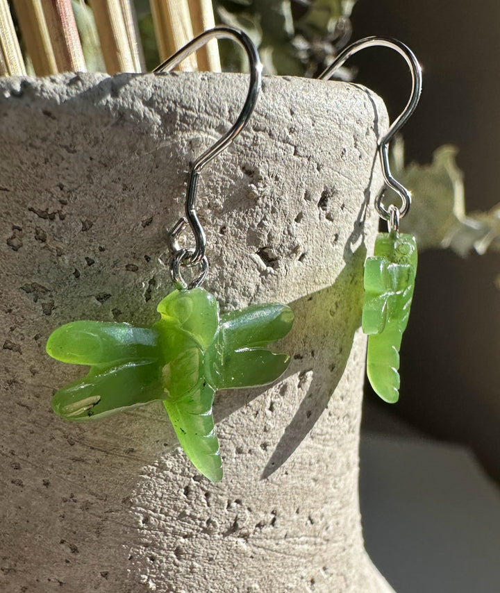 Jade dragonfly earrings with silver hooks resting on a textured concrete surface.