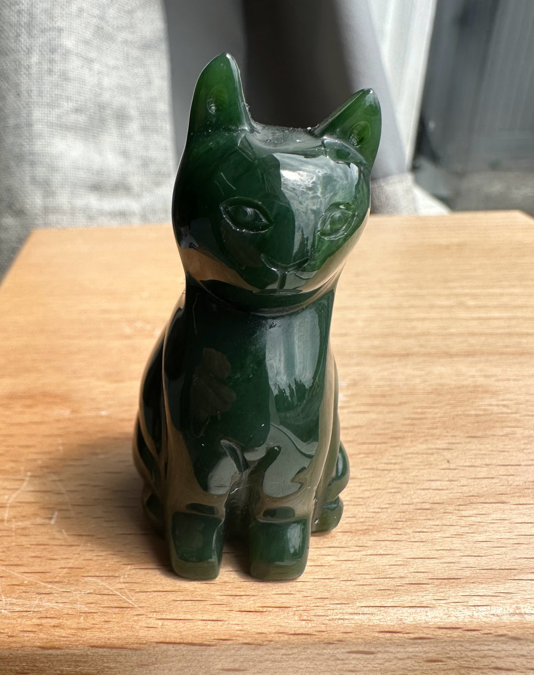 Front view of a dark green jade sitting cat sculpture on a wooden surface.