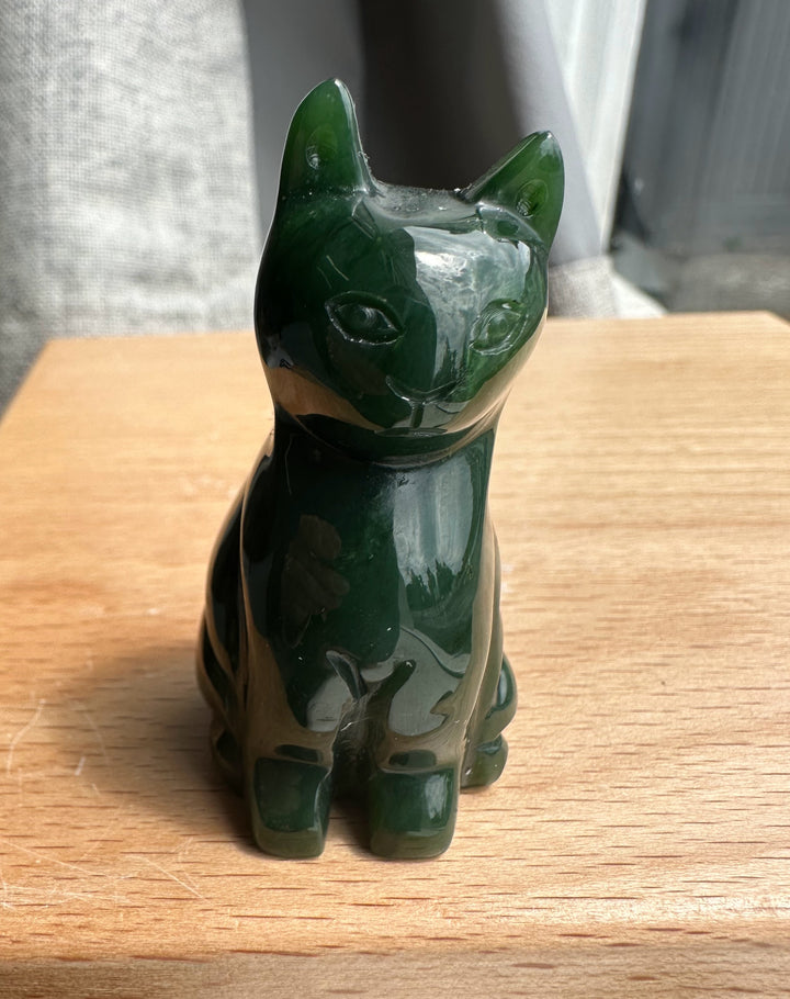 Front view of a dark green jade sitting cat sculpture on a wooden surface.