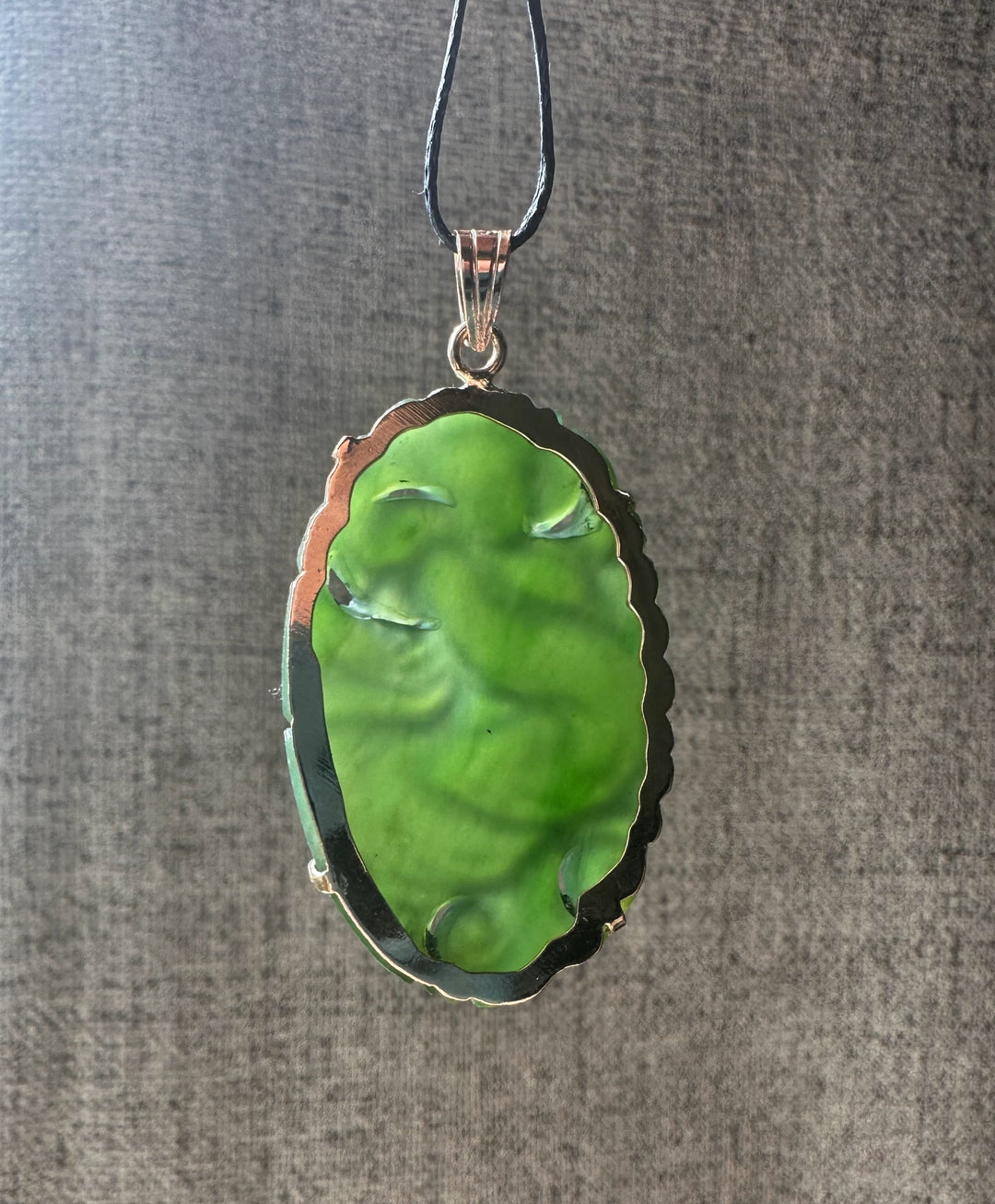 Emerald green jade Guanyin pendant carved with flowing robes and a scalloped metal bezel on a black cord.