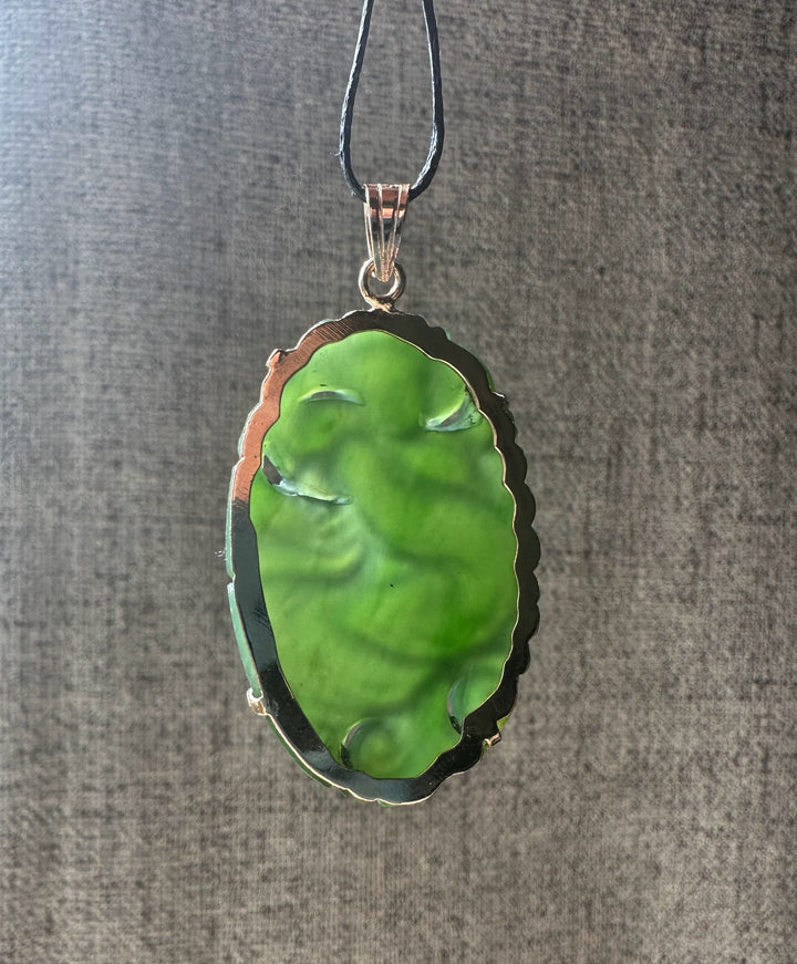 Emerald green jade Guanyin pendant carved with flowing robes and a scalloped metal bezel on a black cord.