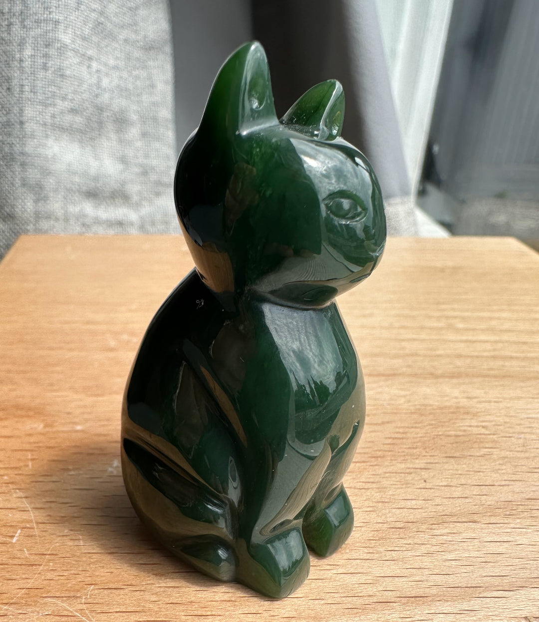 Profile view of dark green jade cat statue with glossy finish on a wooden table