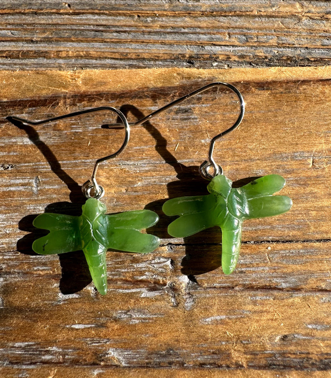 Pair of jade dragonfly earrings with silver hooks on a weathered wooden surface.