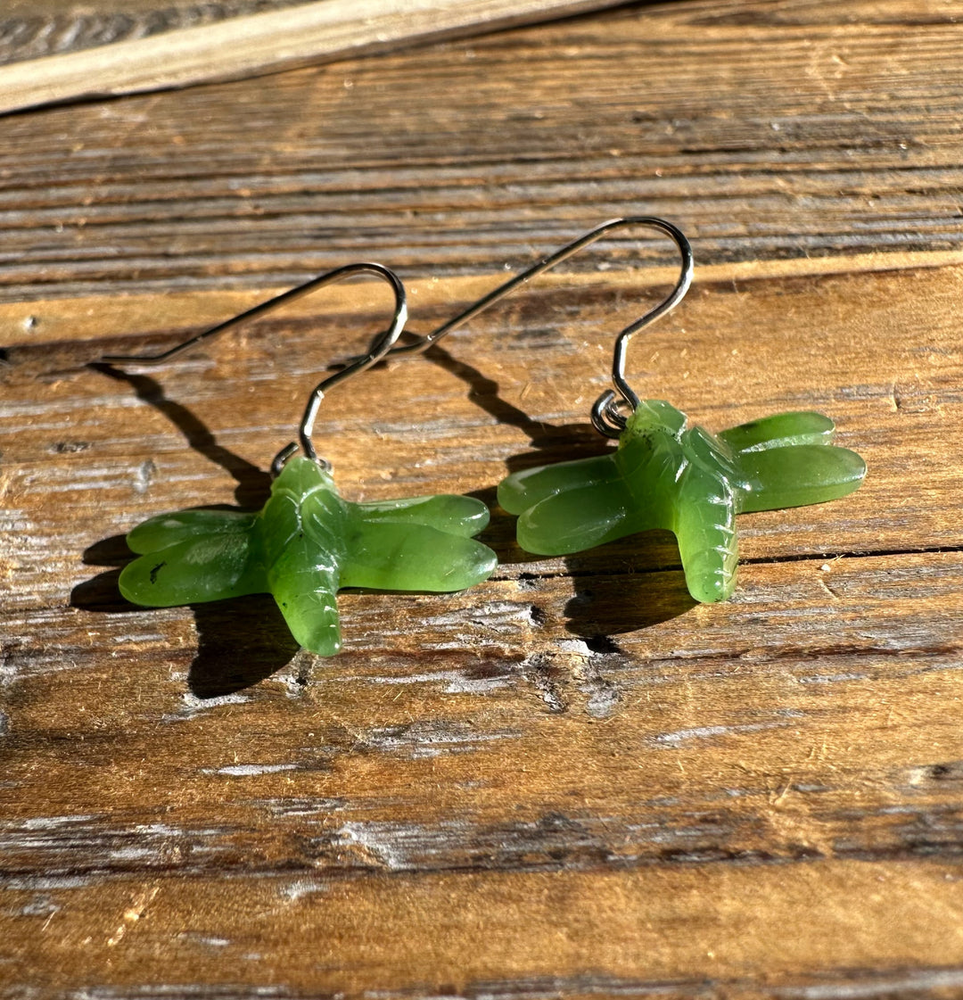 Close-up of jade dragonfly earrings with silver hooks on rustic wooden planks.