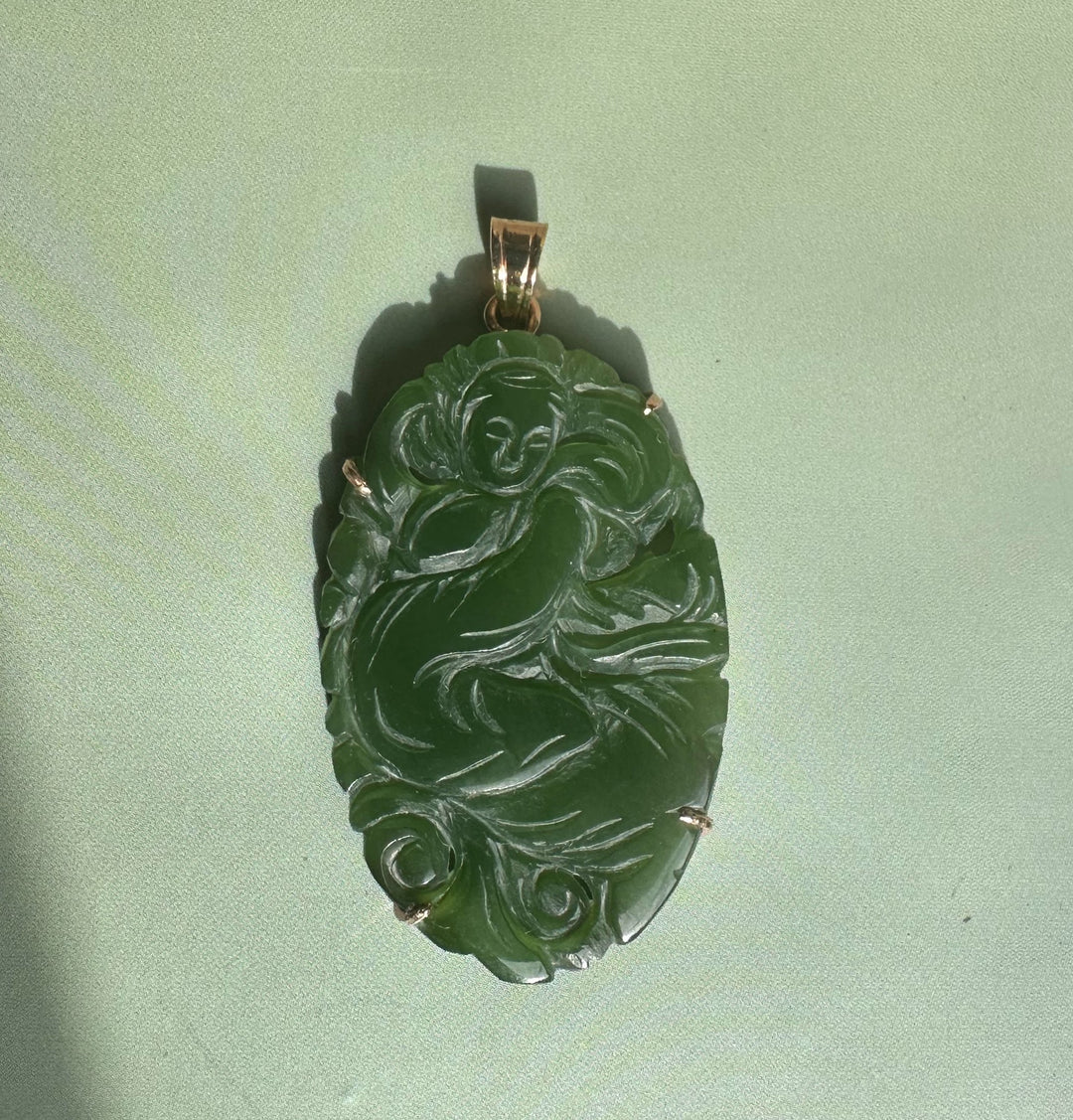 Emerald green jade Guanyin pendant with intricate swirling carving and gold bail