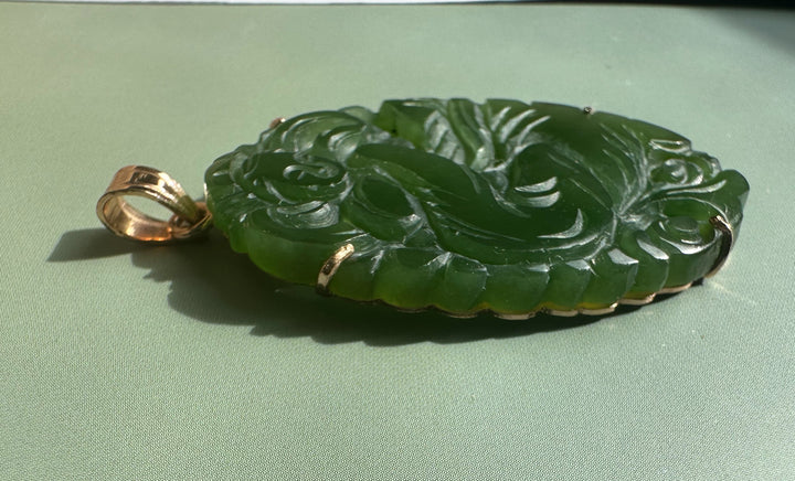 Side view of vintage jade Guanyin pendant showing ornate carved surface and gold bail