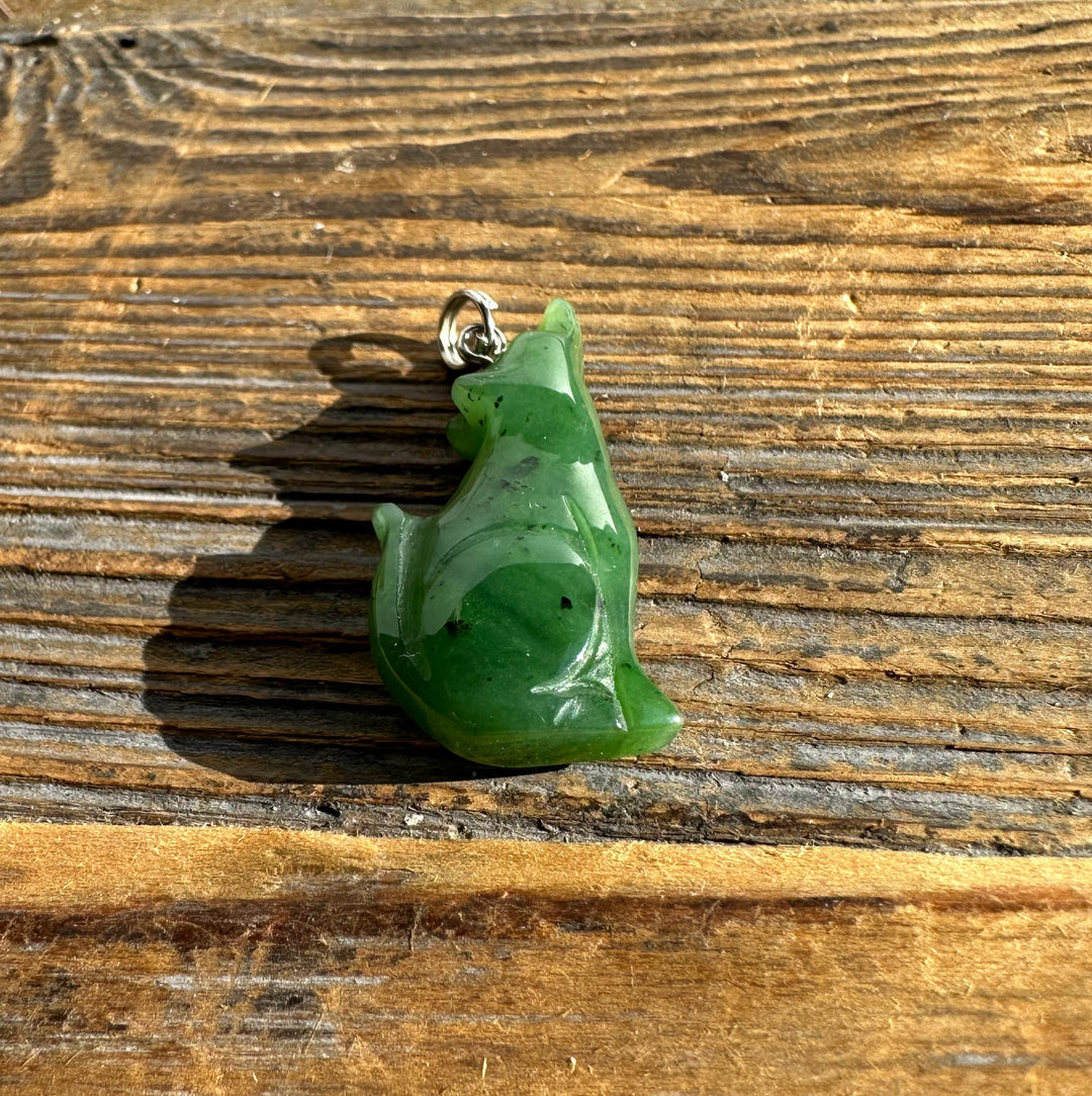 Close up of jade wolf pendant with silver bail on a wood background