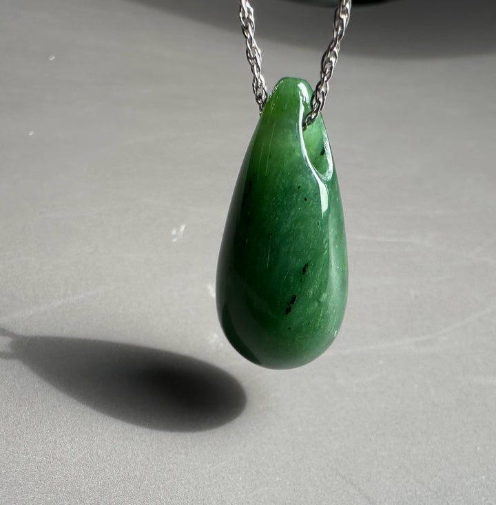 Close up of a green jade teardrop pendant on a silver chain against a gray background