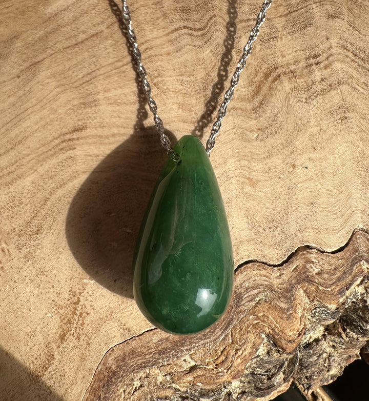 Green jade teardrop pendant on a silver chain resting against a wooden background.