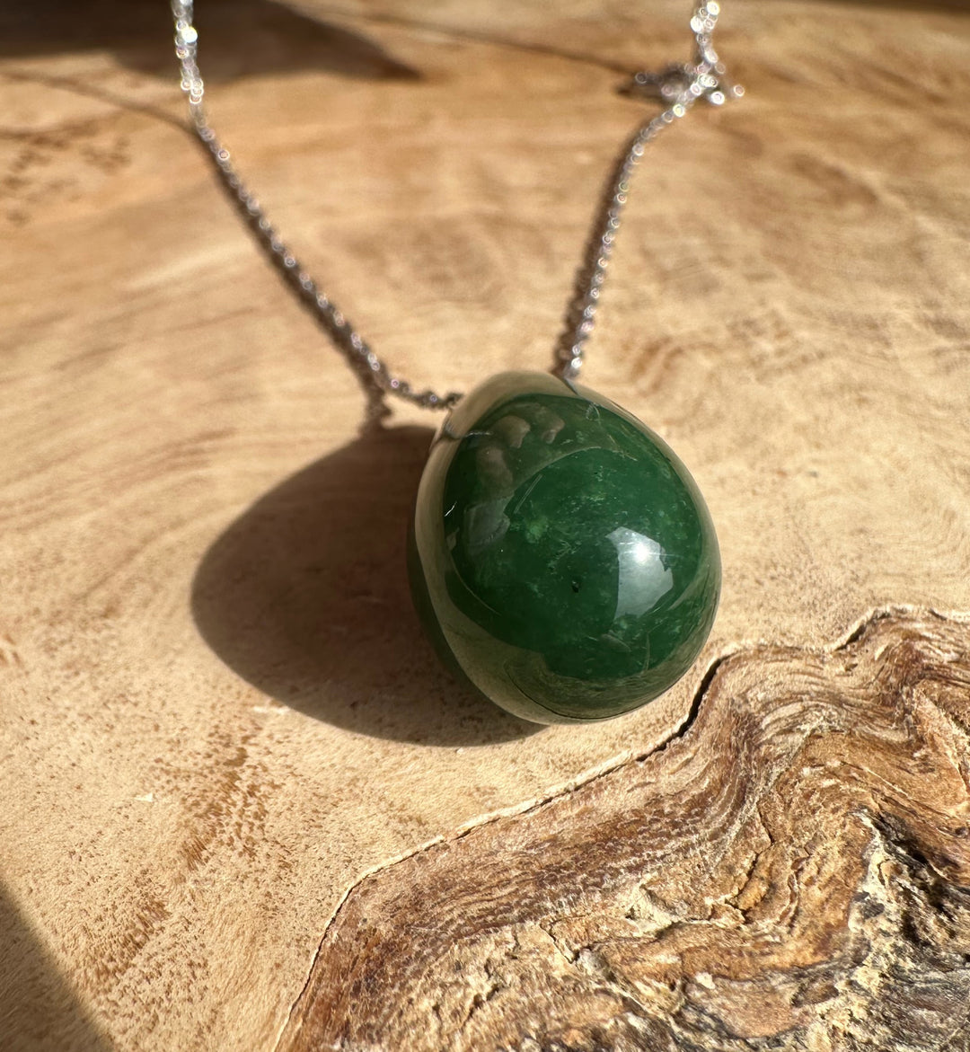 Jade teardrop pendant on a silver chain resting on a wooden surface