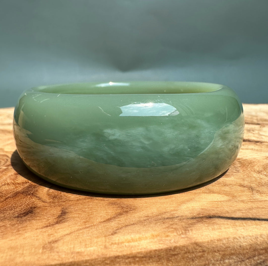 Green glossy Siberian jade bangle shown from a side angle on a wooden surface.