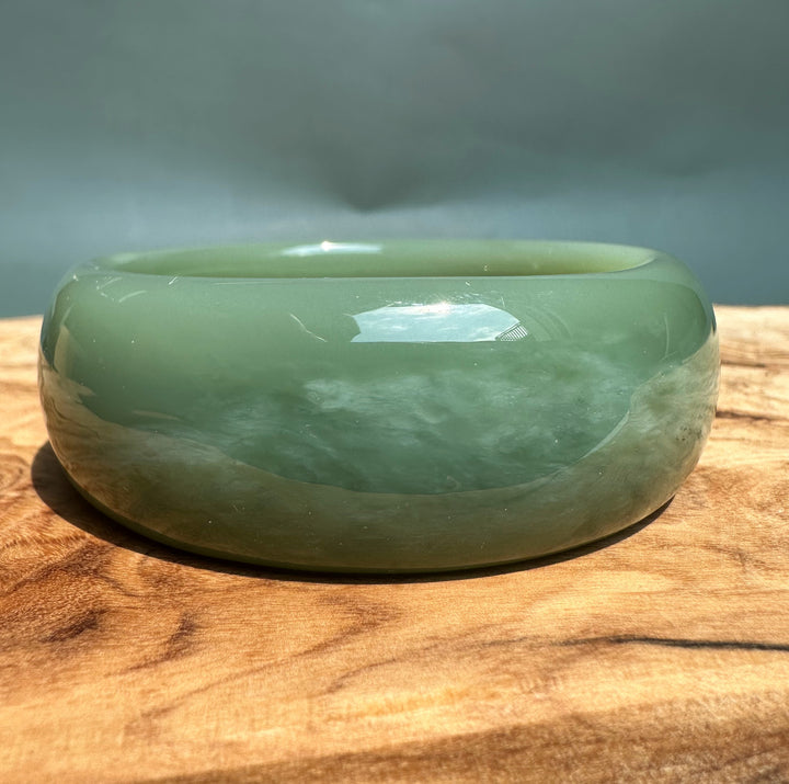Green glossy Siberian jade bangle shown from a side angle on a wooden surface.