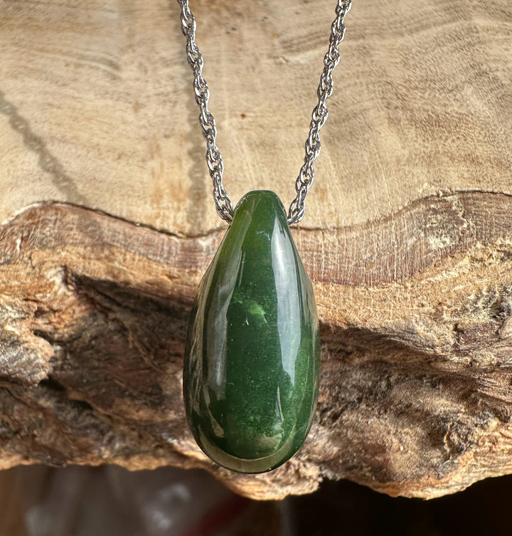 Dark green Canadian jade teardrop pendant on a silver chain against a wooden backdrop.