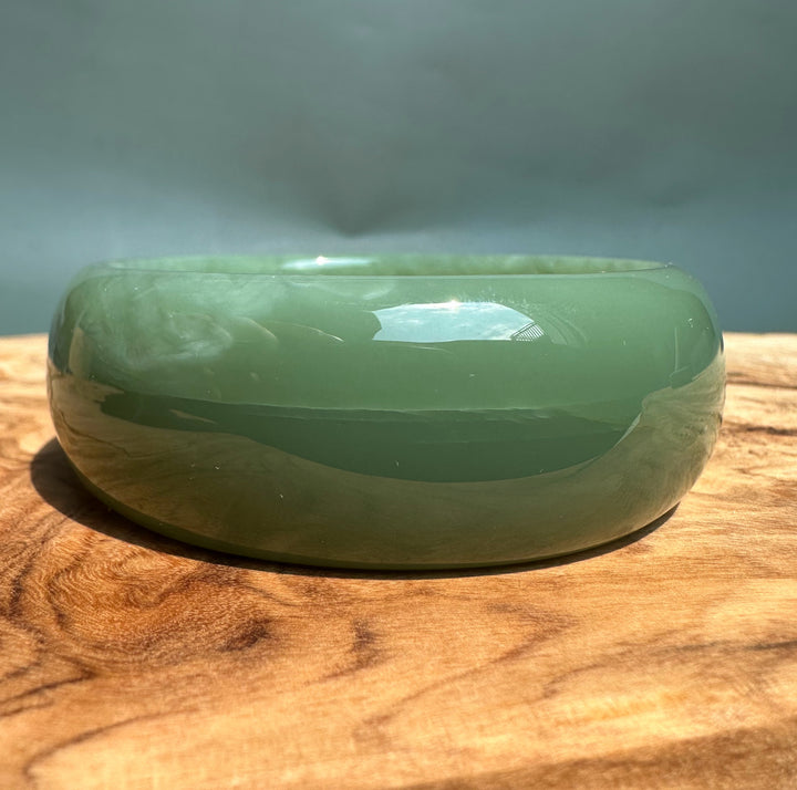 A Grade Siberian Bangle green jade with glossy finish resting on a wooden surface.