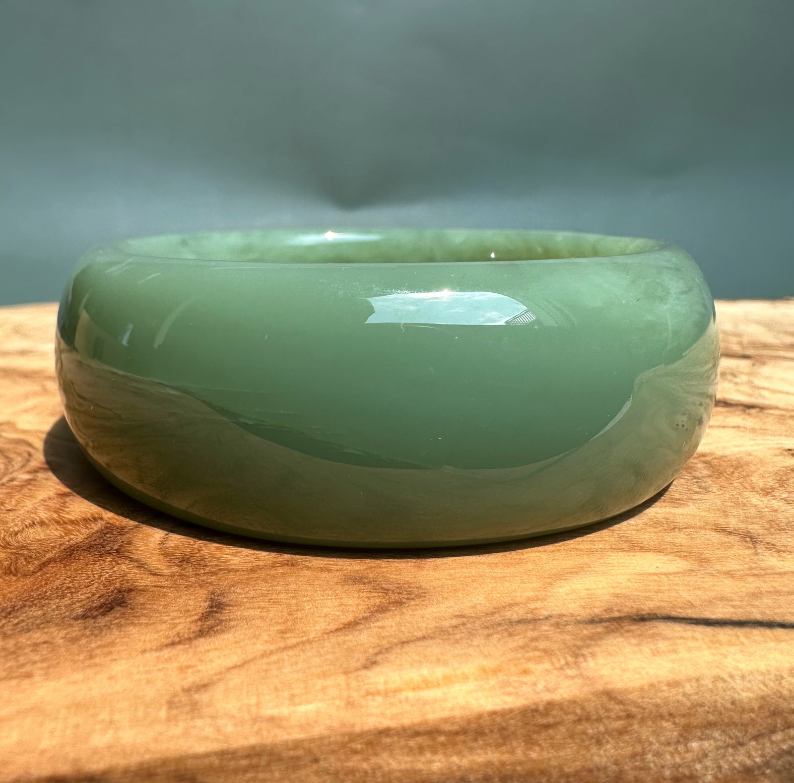 Green glossy Siberian jade bangle resting on a wooden surface.