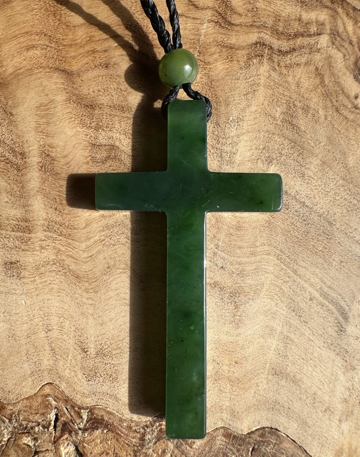 Close up of green jade cross pendant on black braided cord with bead at the top