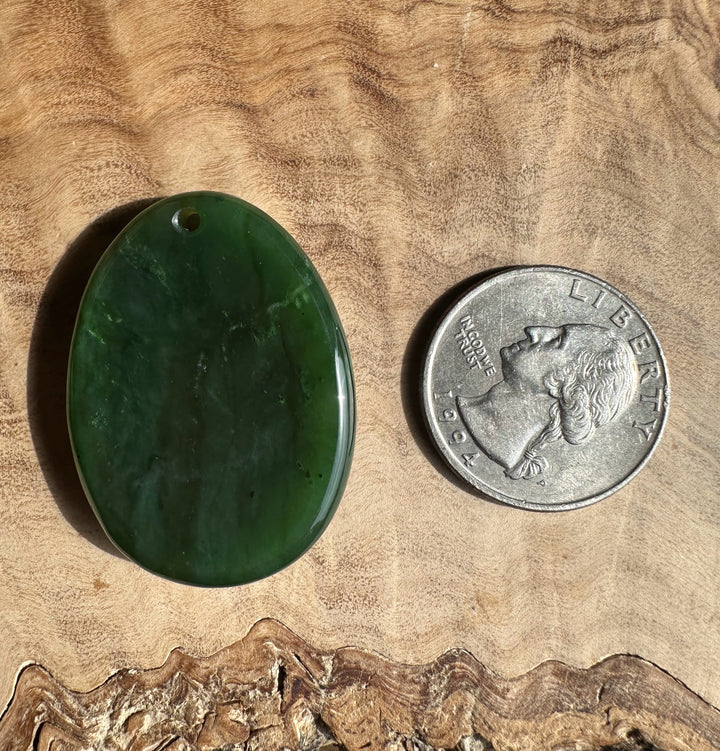 Green stone pendant next to a U.S. quarter on a wooden surface