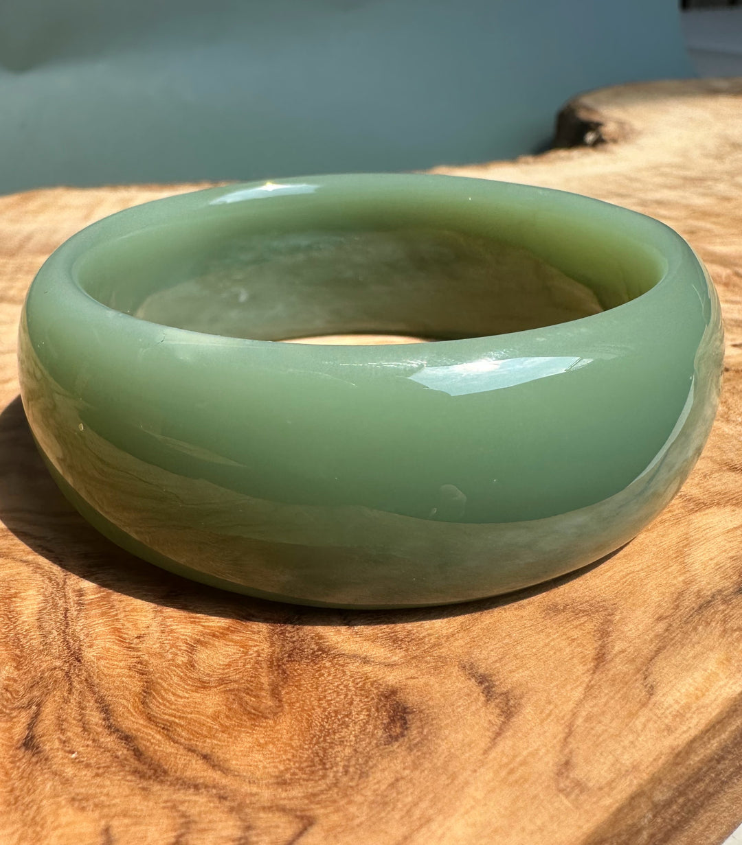 A Grade Siberian jade bangle in pale green resting on a wooden surface.