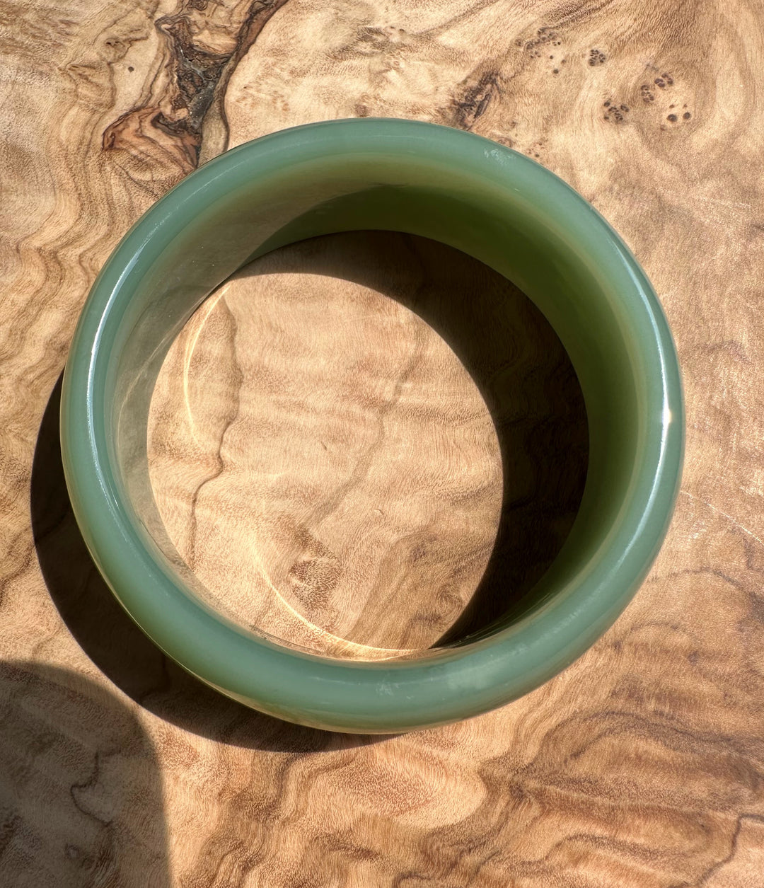 Top view of a pale green Siberian jade bangle on a wooden surface, size 57.5 x 23mm.