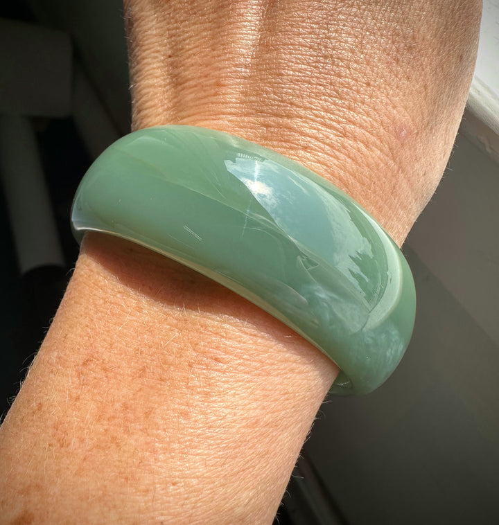 A Grade Siberian Bangle in pale green jade worn on the wrist with a polished curved surface.