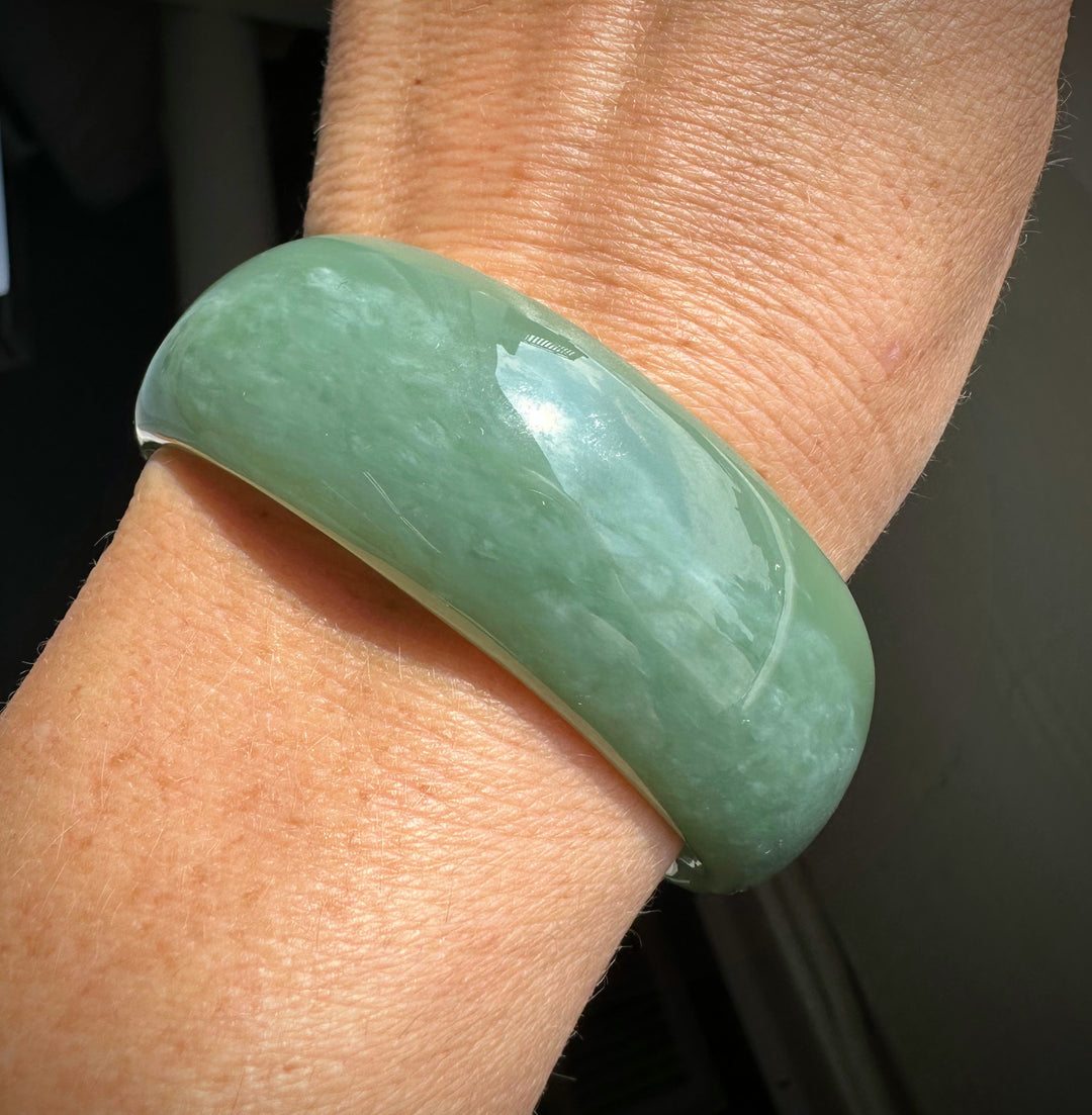 Close up of pale green jade bangle on the wrist showing the smooth glossy surface.