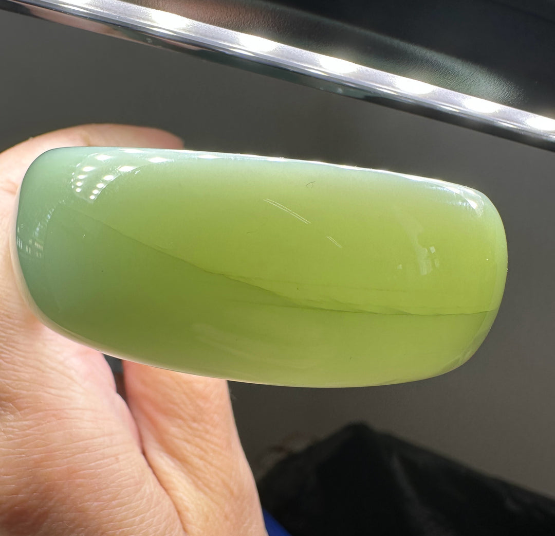 Close up of a green jade bangle held by fingers showing a seam and polished surface.