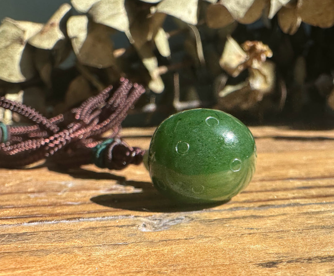Side view of green jade mushroom pendant on a brown cord against a textured concrete background