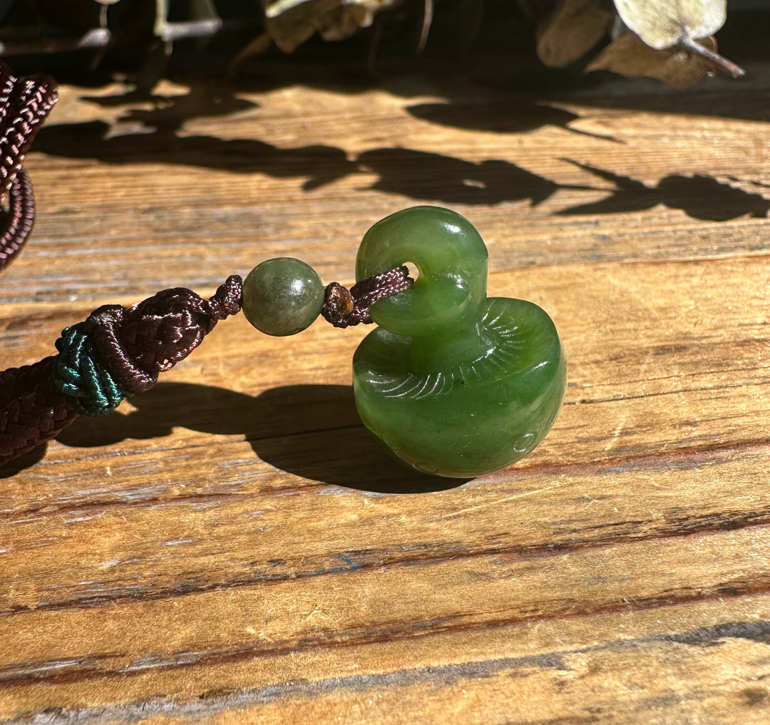Green jade mushroom pendant with a donut shaped ring on a braided cord resting on a wooden surface