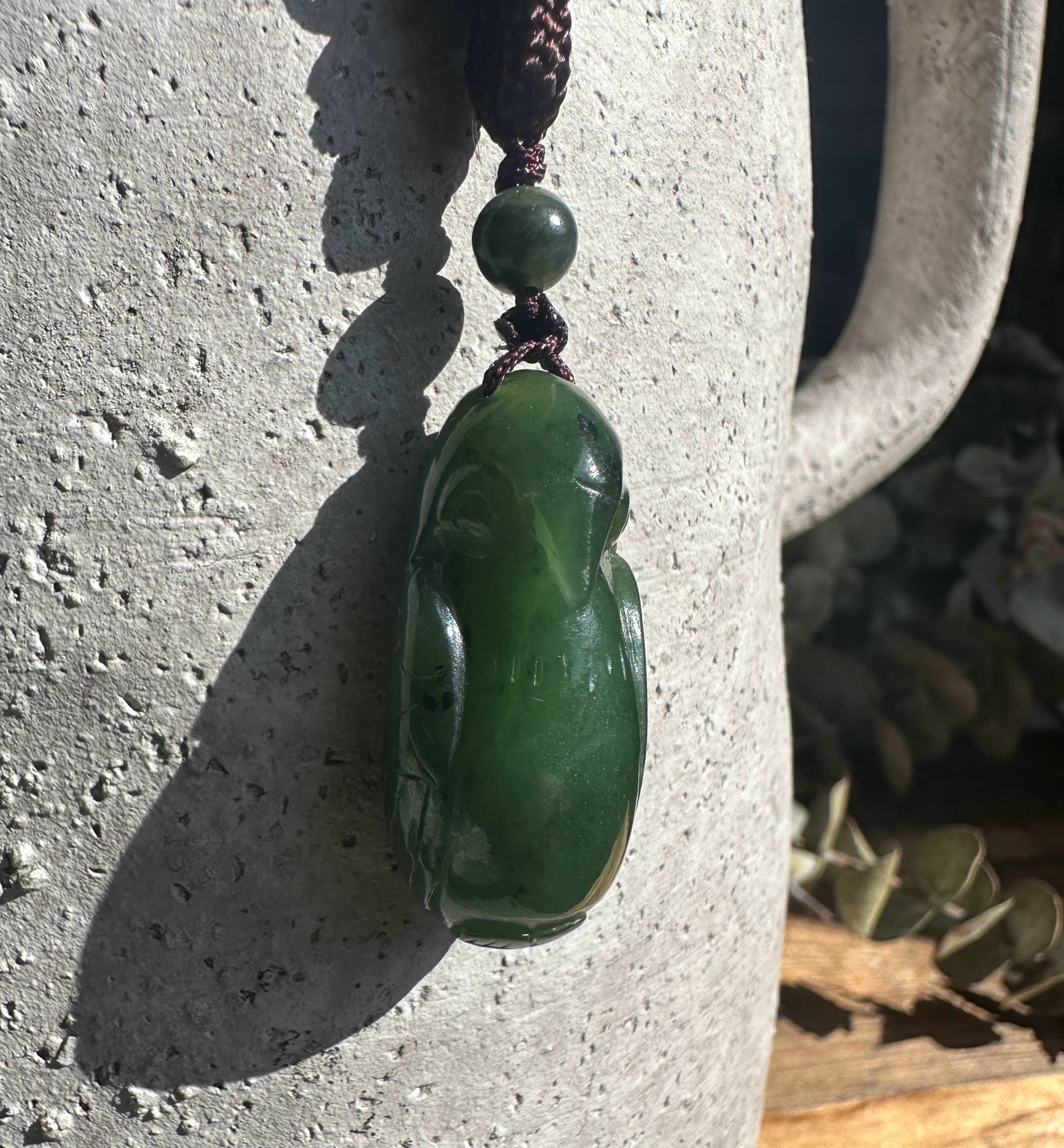 34mm Jade bird pendant hanging on a dark cord against a textured stone surface.