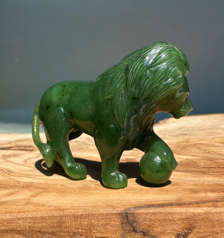 Side view of a green jade lion statue with a paw resting on a ball