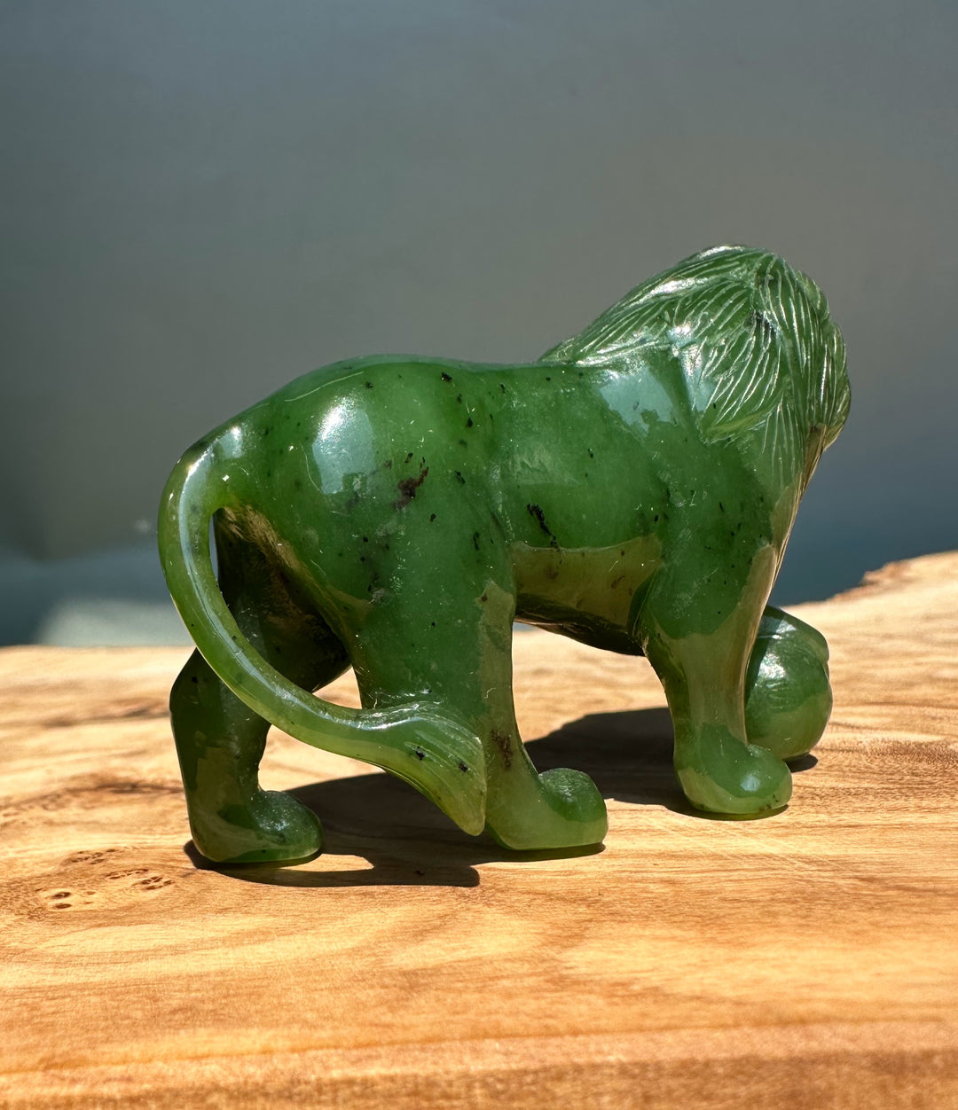 Side view of green jade lion with flowing mane on a wooden surface