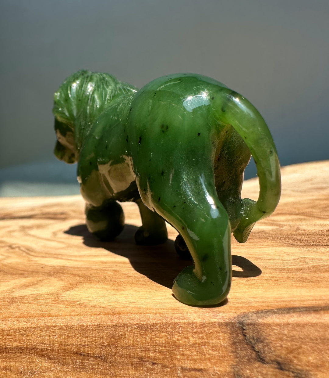 Rear view of green jade lion showing hind legs and tail on a wooden surface