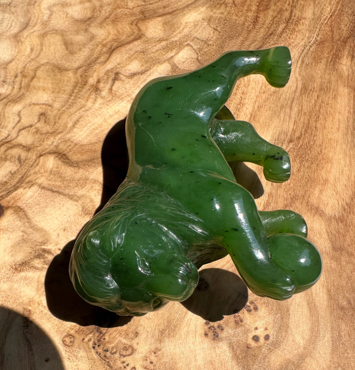 Green Canadian jade lion sculpture resting on a wooden surface.