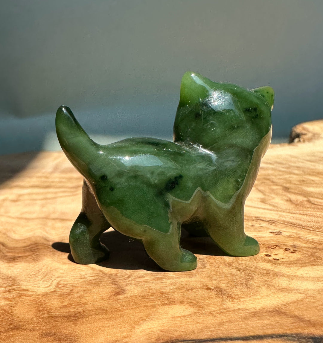 Glossy Canadian Jade cat figurine with raised tail on a wooden surface.