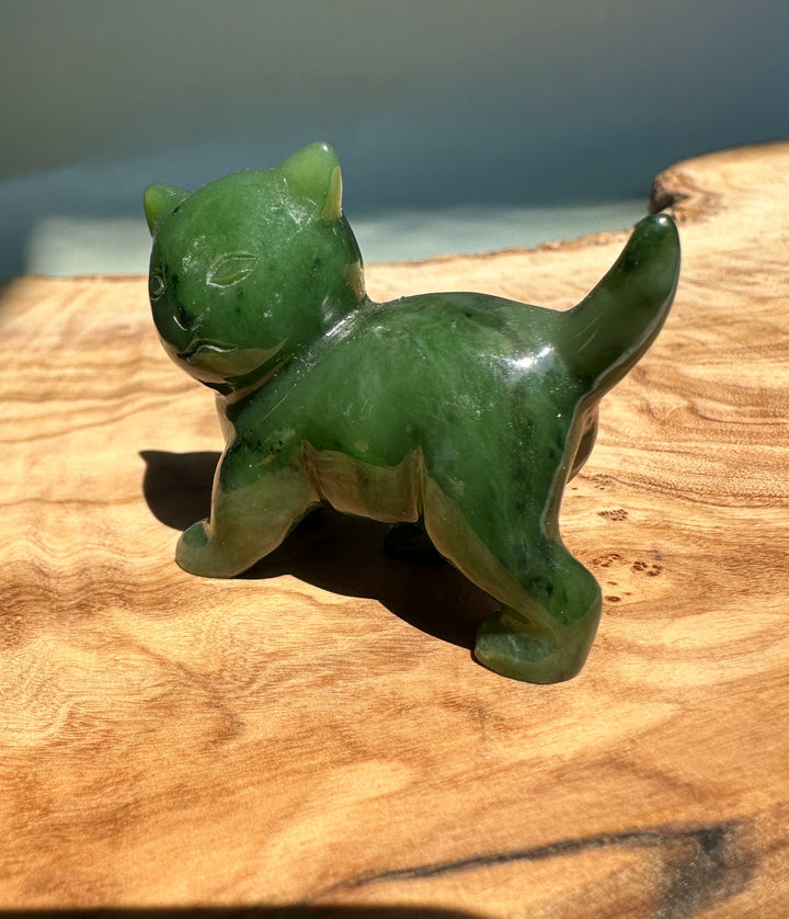 Side view of glossy Canadian Jade cat figurine with curved tail on a wooden surface.