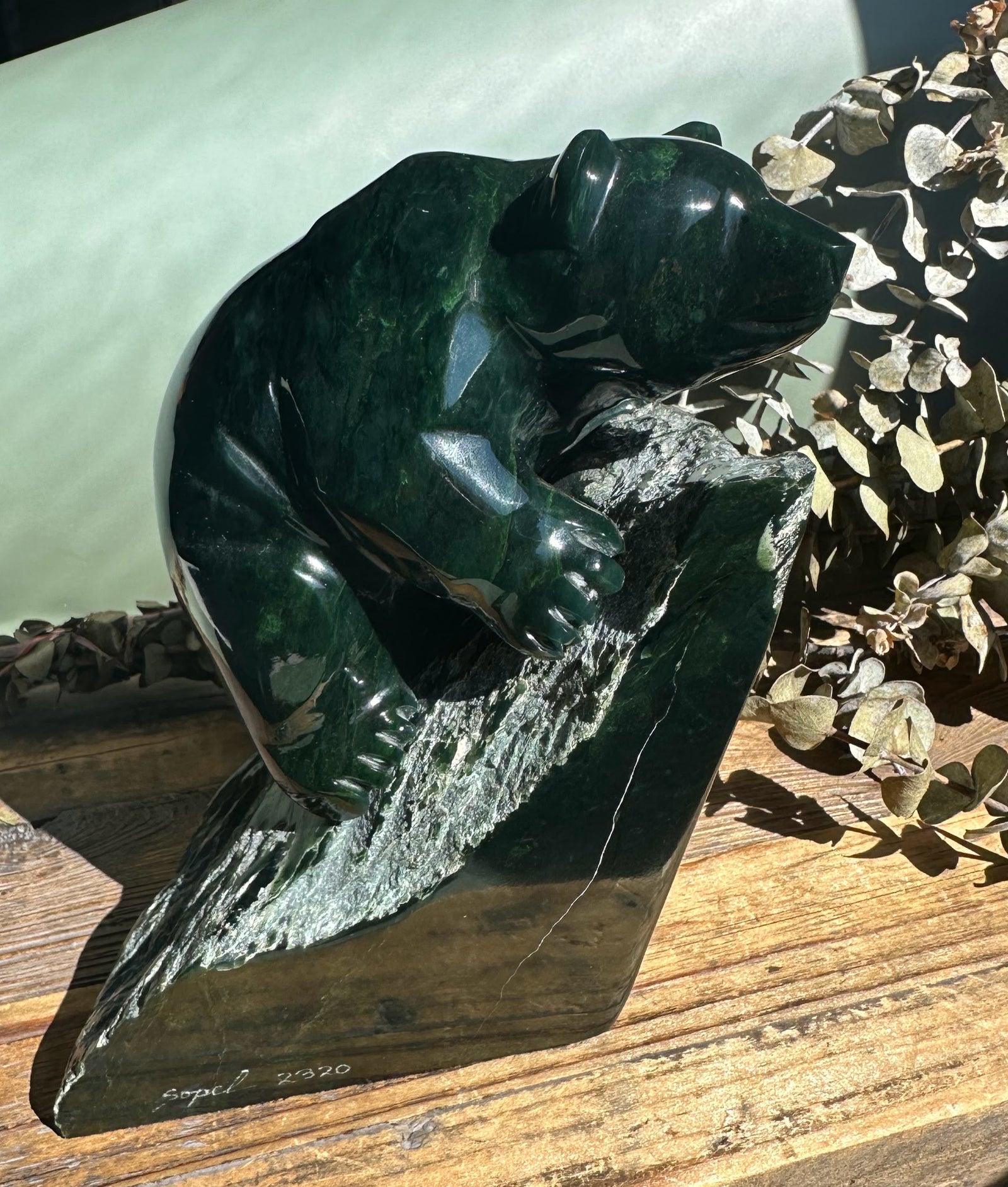 Dark green Ogden jade bear by Lyle Sopel perched on a textured stone pedestal.