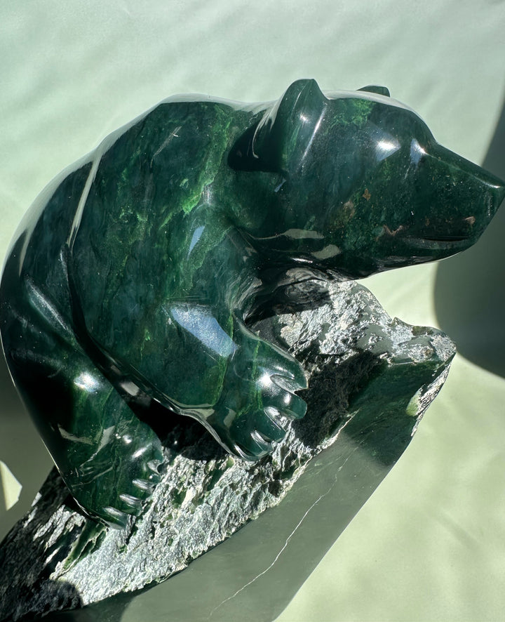 Side view of dark green Ogden jade bear sculpture by Lyle Sopel on a textured rock base