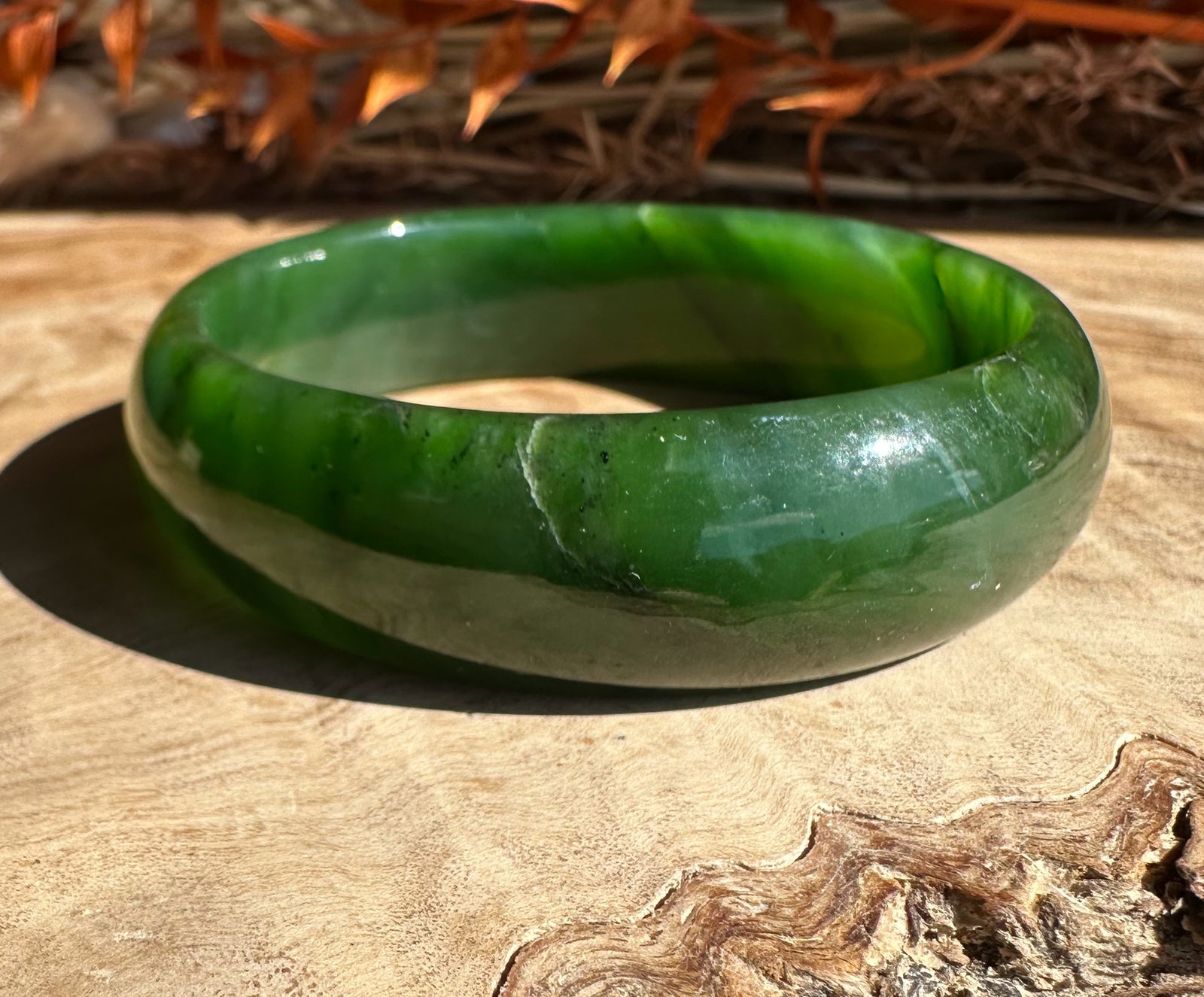 Jade bangle in various green tones with white streaks on a wooden surface.