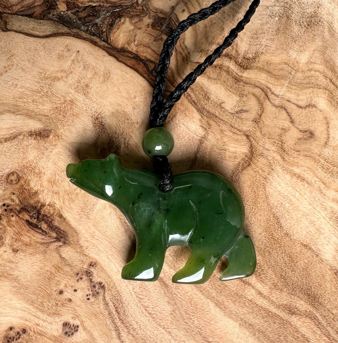Green jade bear pendant on black braided cord with bead shown on a textured wood background