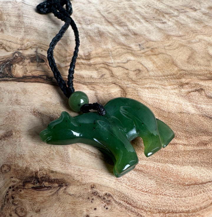 Green jade bear pendant on a black braided cord with a round green bead against wood grain