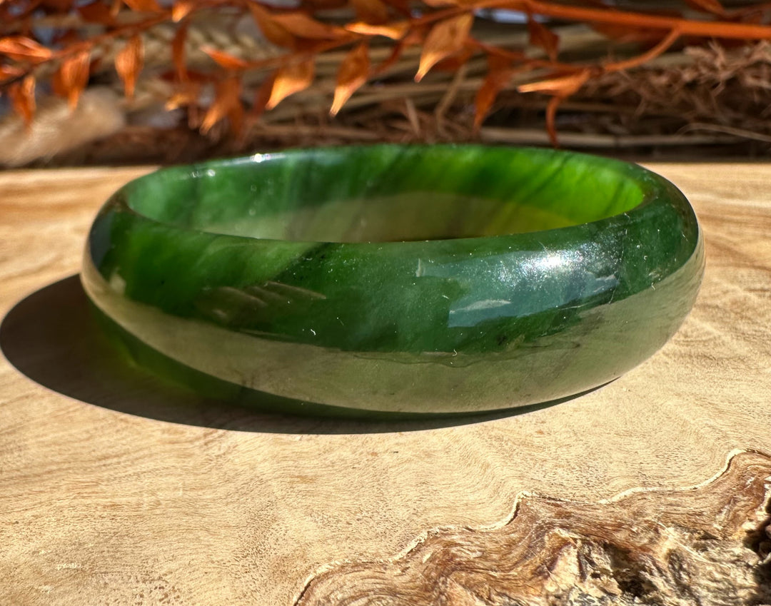 Polished green jade bangle 58 x 16.5 mm resting on a sunlit wooden surface.