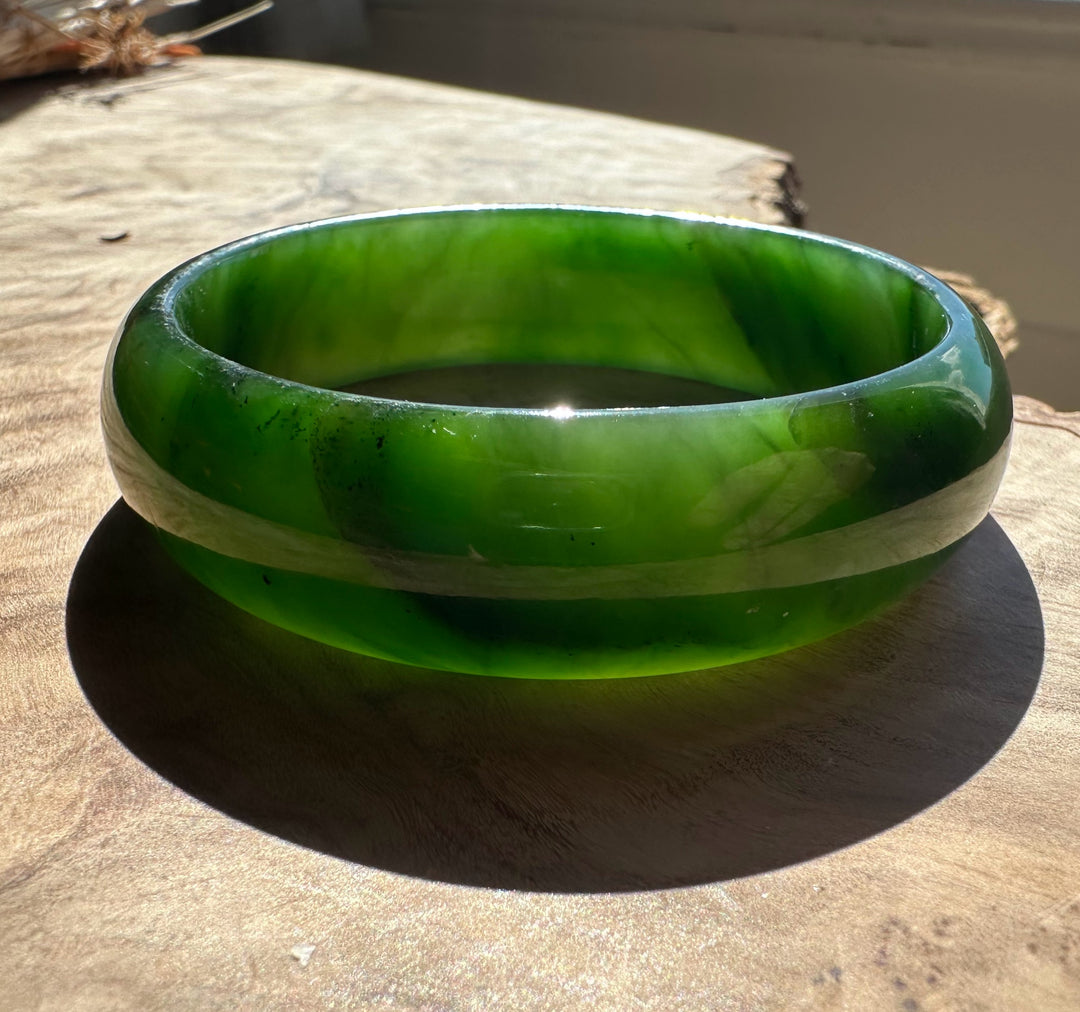 Vivid green jade bangle with a pale central band on a wooden surface.