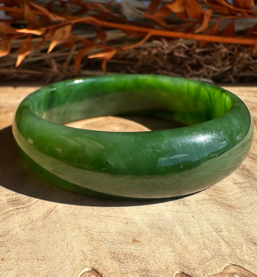 Close up of green jade bangle with a lighter band against a sunlit wooden backdrop.